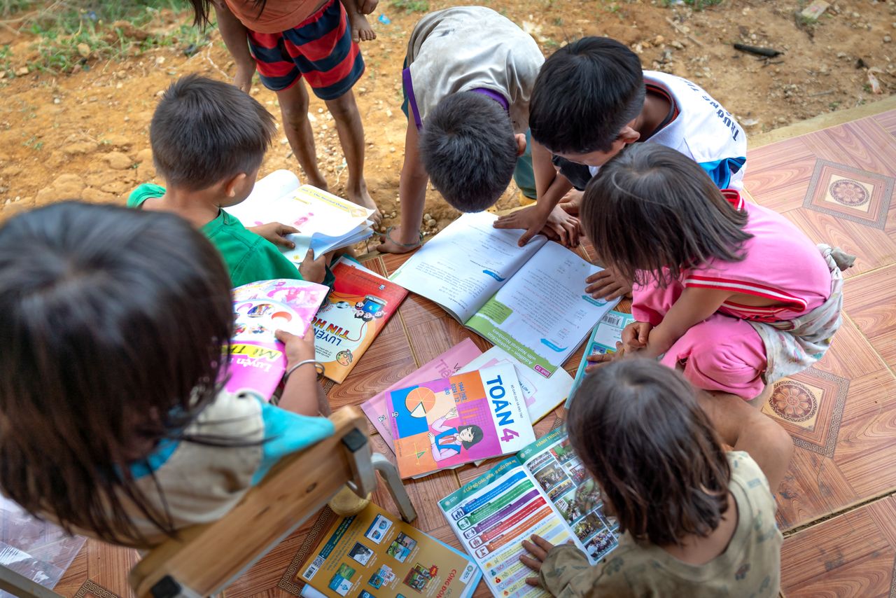 Children gathered outdoors, actively engaged in reading and learning from books.