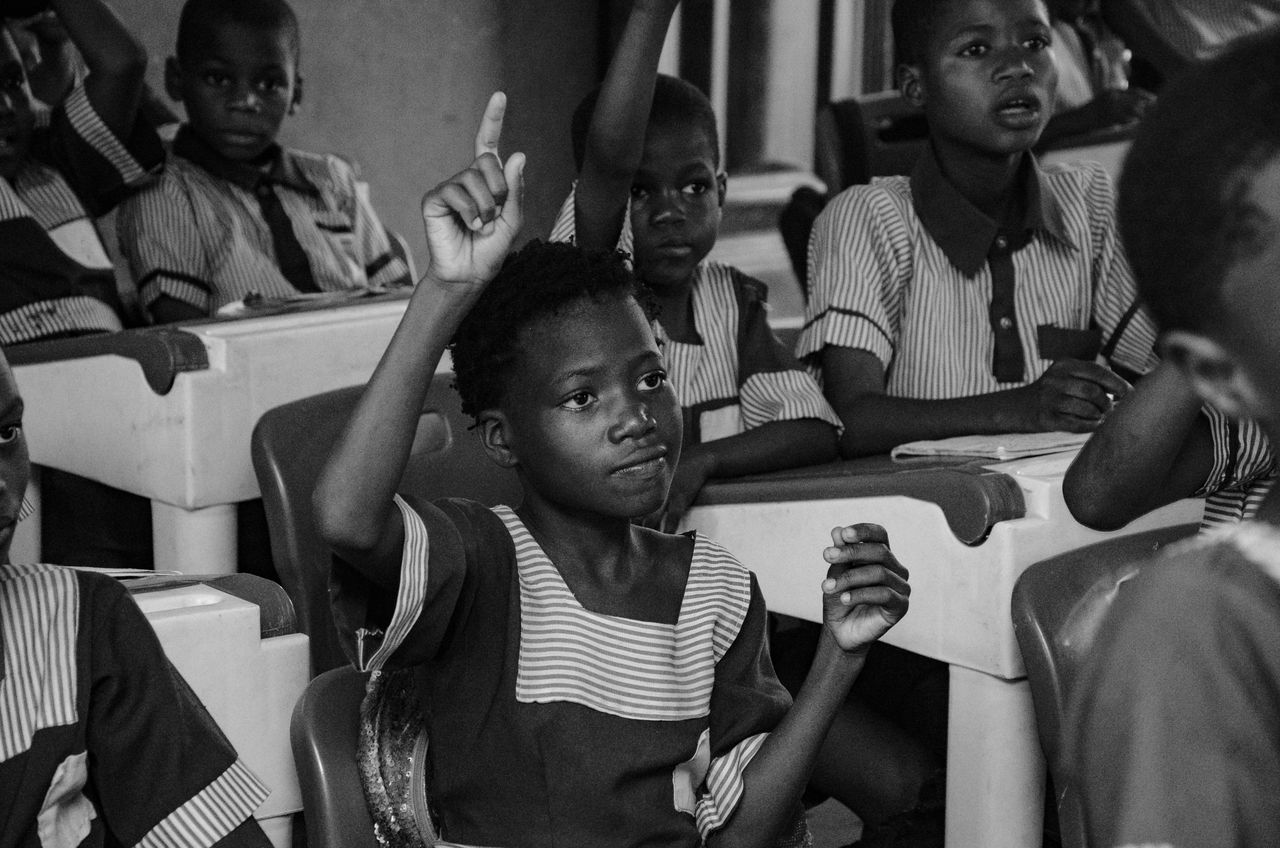 Black and white photo of students actively participating in a classroom lesson, raising hands to ask questions.